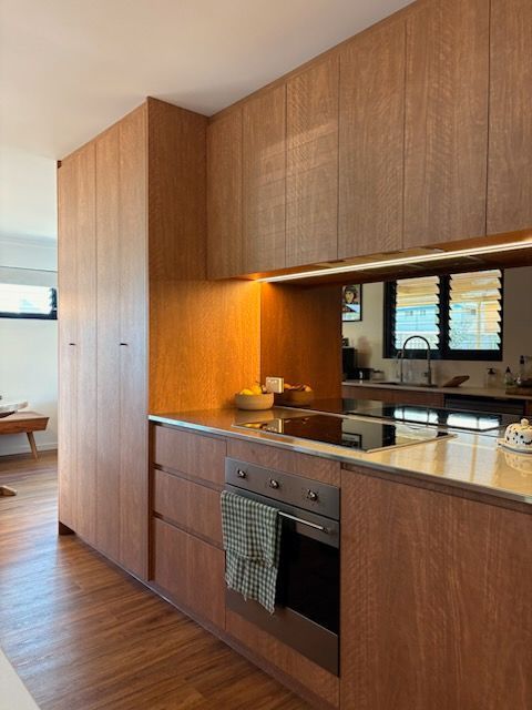 Modern Kitchen with Wood Cabinetry, Built In Oven, and Black Countertop — JPR Concepts in Burleigh Heads, QLD