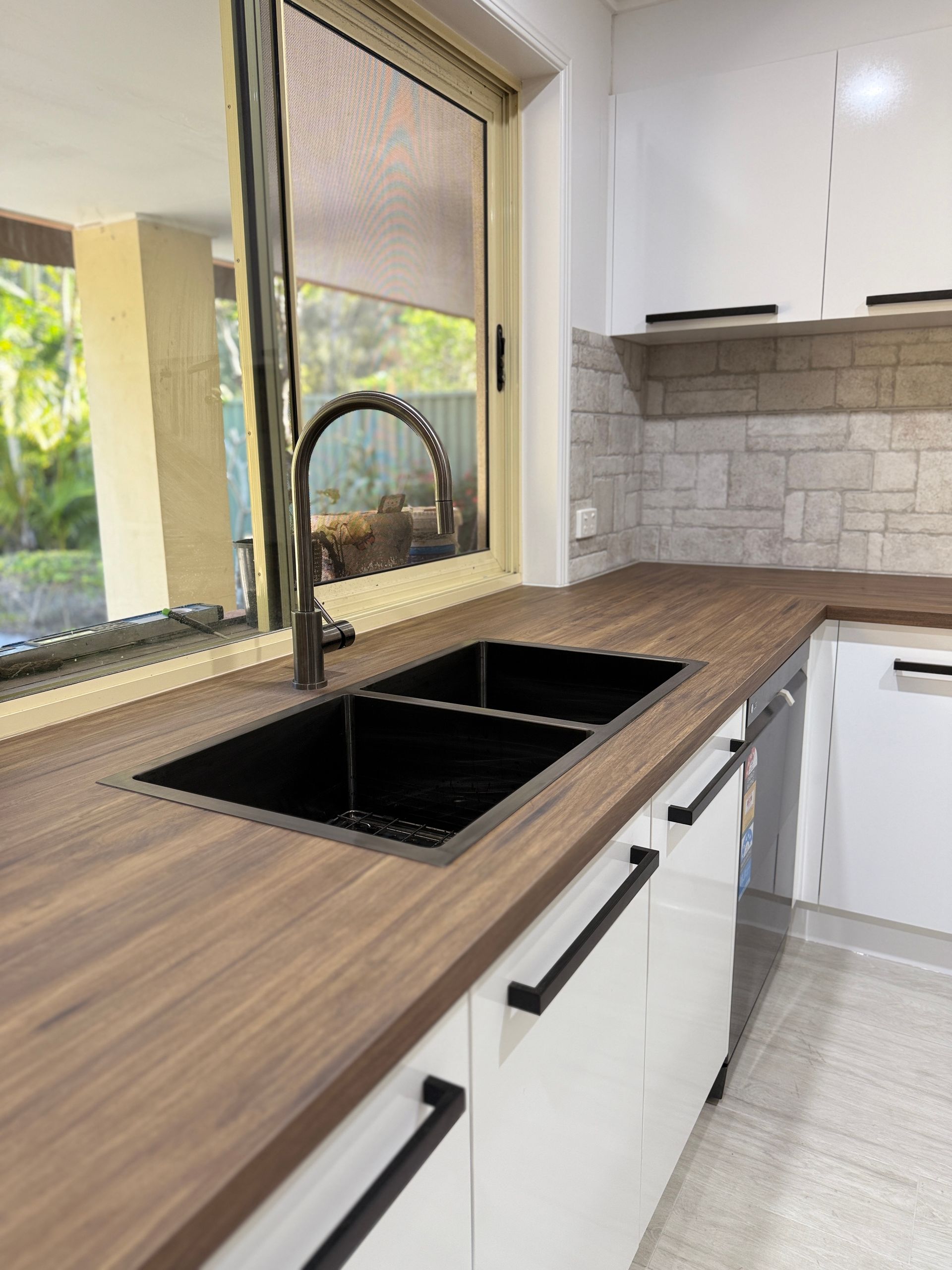Modern Kitchen with Black Sink and Faucet, White Cabinets, Wood Countertop, and Window — JPR Concepts in Burleigh Heads, QLD