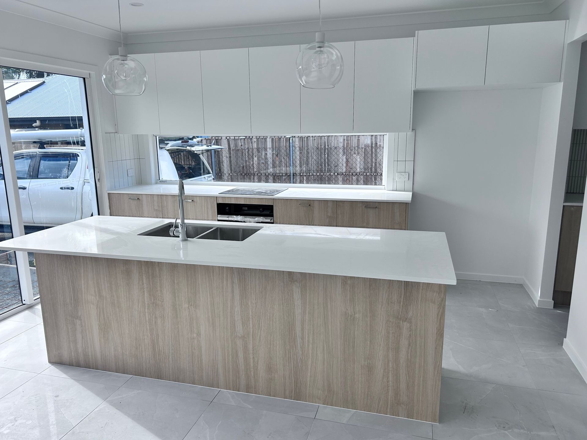 Modern White Kitchen with A Large Island, Wood Paneling, and Pendant Lights — JPR Concepts in Burleigh Heads, QLD