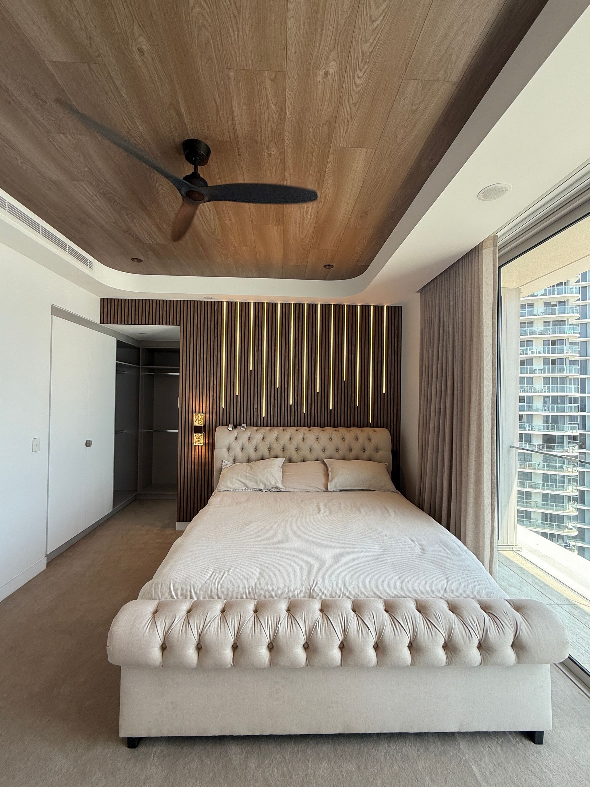 Modern Bedroom with Tufted Cream Bed, Wood Ceiling and Striped Accent Wall — JPR Concepts in Burleigh Heads, QLD