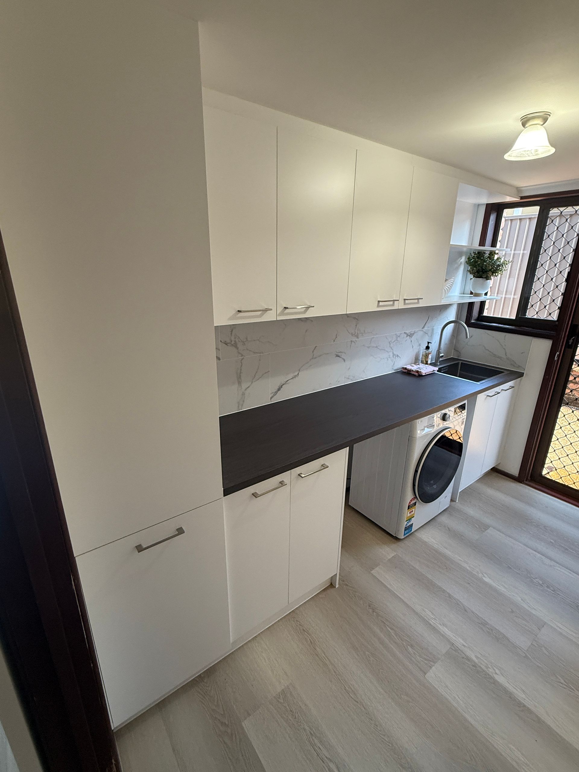 Narrow Laundry Room with White Cabinets and Black Countertop — JPR Concepts in Burleigh Heads, QLD