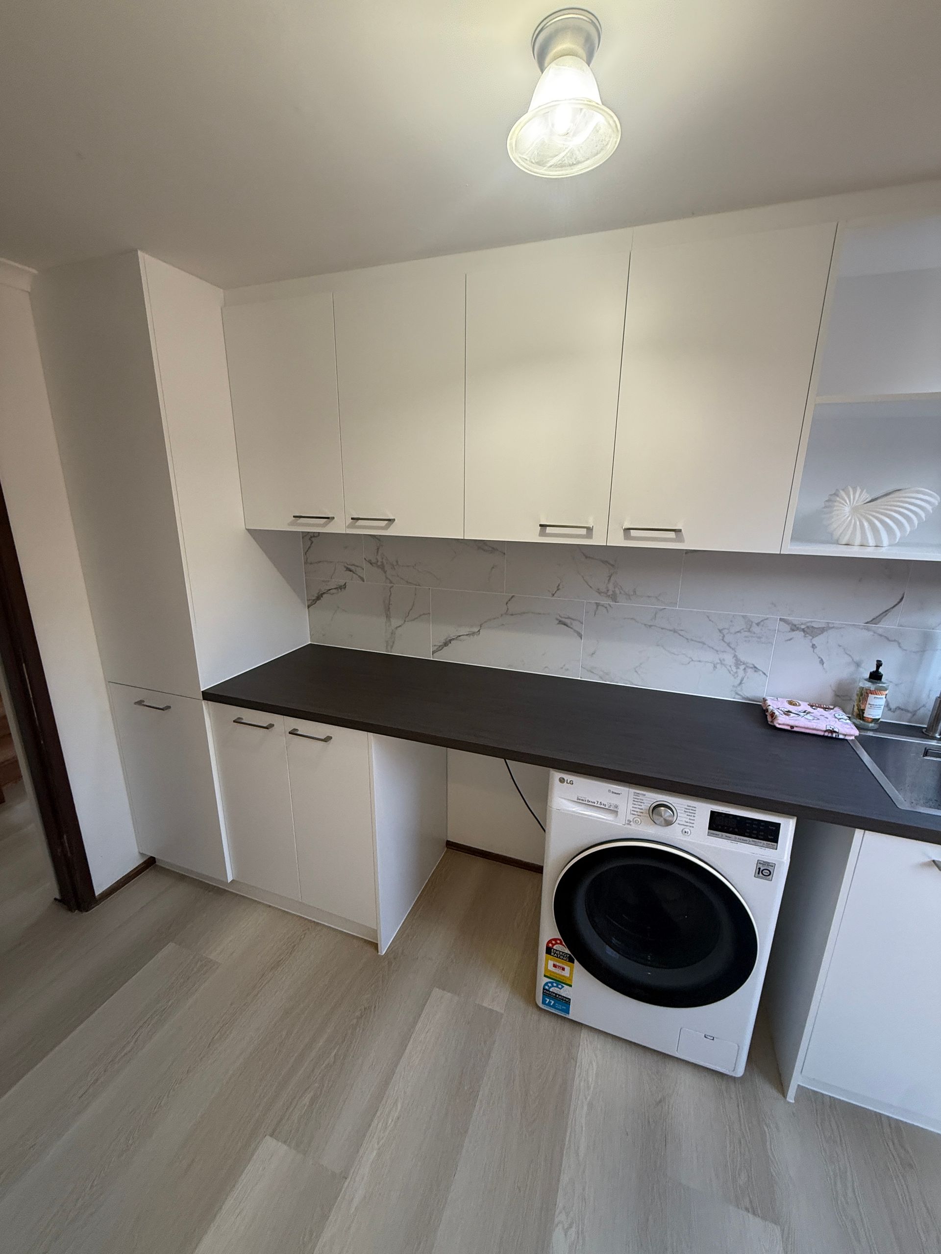 Small Laundry Room with White Cabinets and Black Countertop — JPR Concepts in Burleigh Heads, QLD