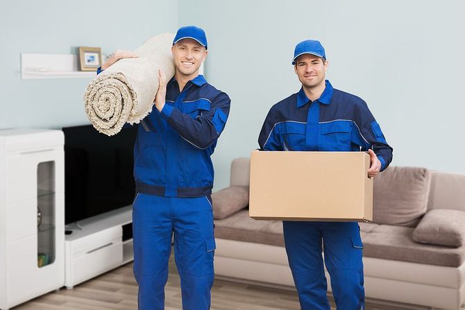 Two smiling movers holding a rolled rug and a box.