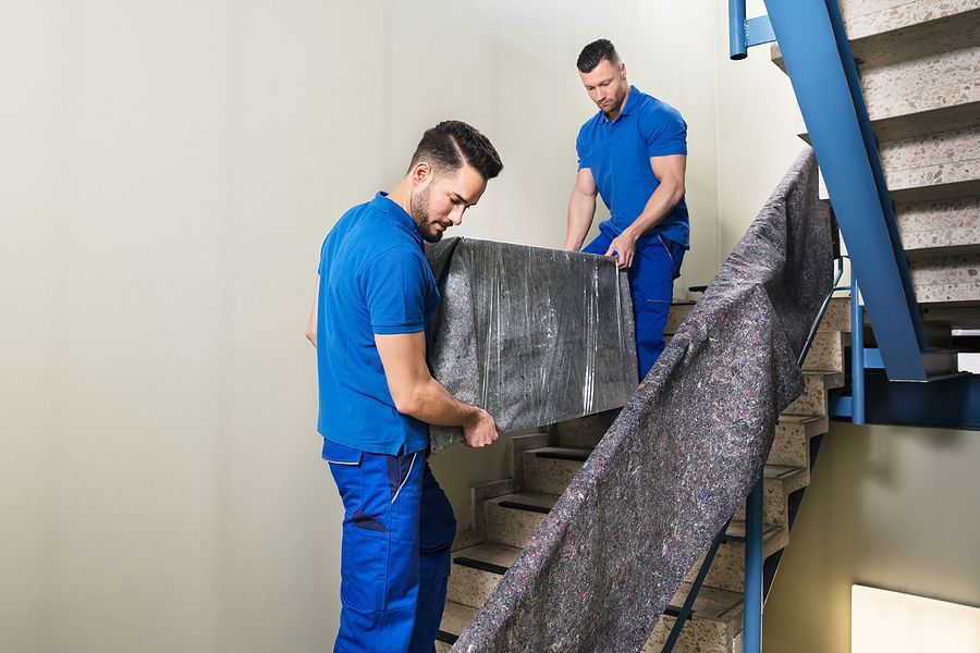 Two movers carefully carrying a wrapped item up stairs.