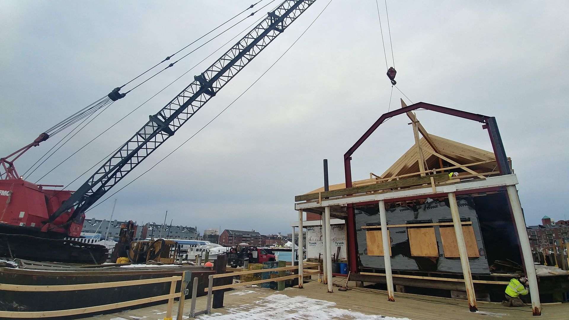 Construction crane lifting roof beams onto a building frame under overcast sky