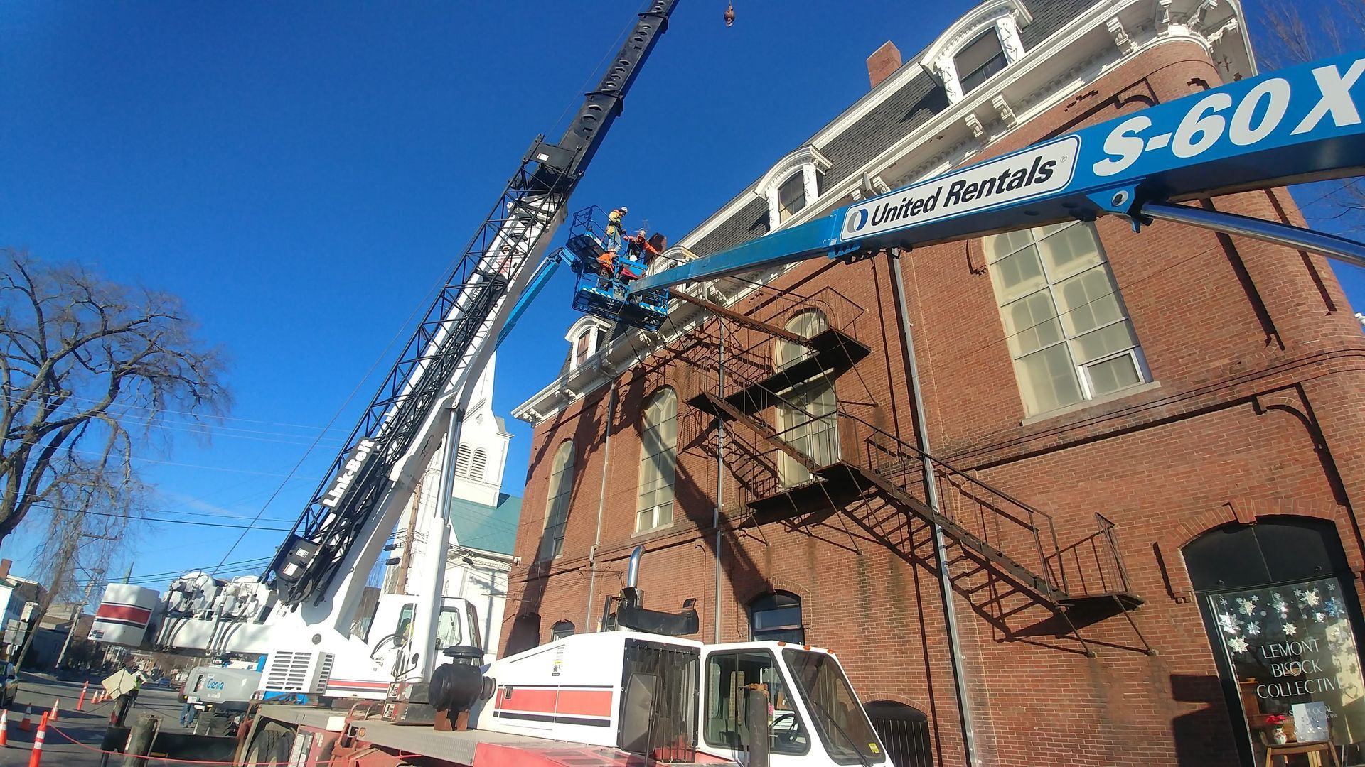 Crane and boom lift working on a brick building under a clear blue sky