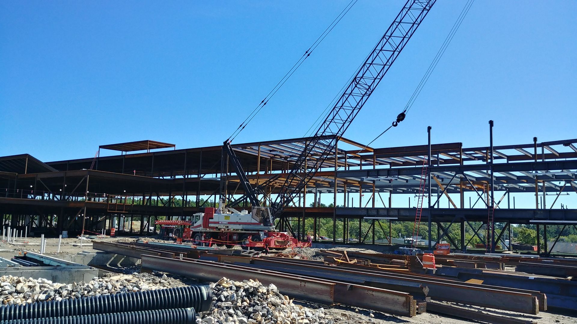 Construction site with steel framework, cranes, and workers under a clear blue sky
