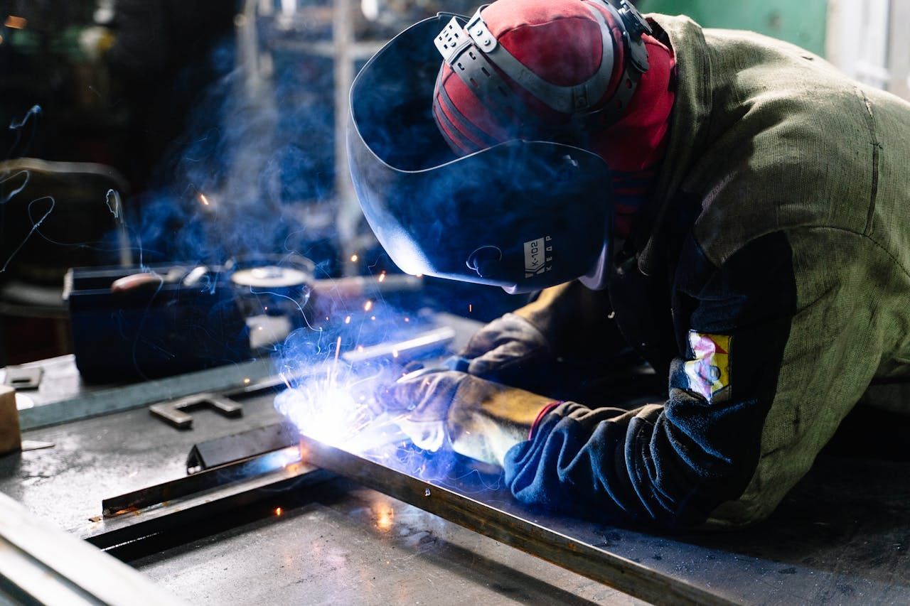 A man is welding a piece of metal in a factory.