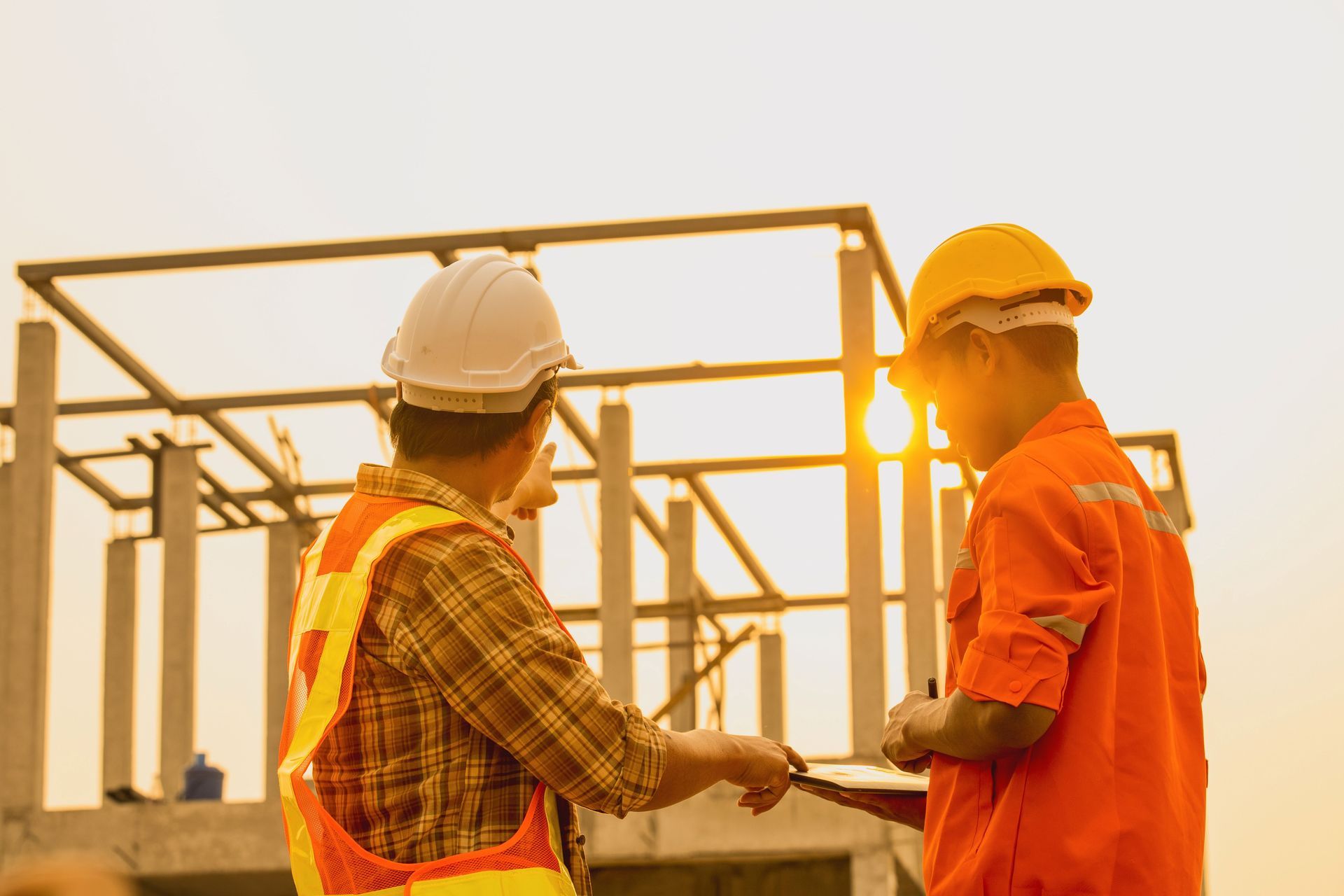 Two construction workers are standing in front of a building under construction.