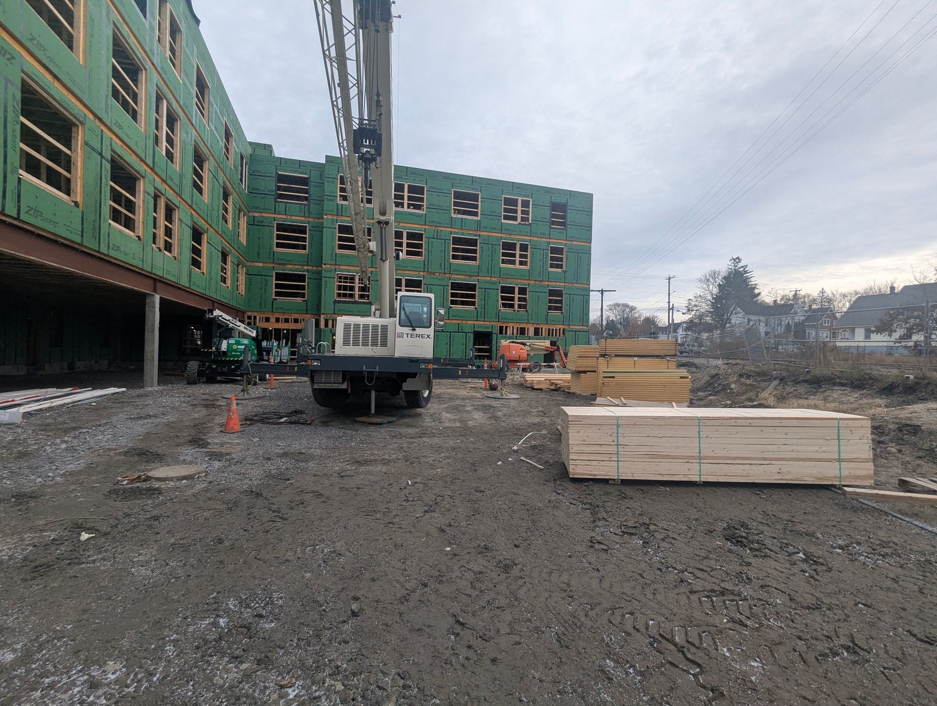 Construction site with a green building, crane, and stacked lumber under an overcast sky