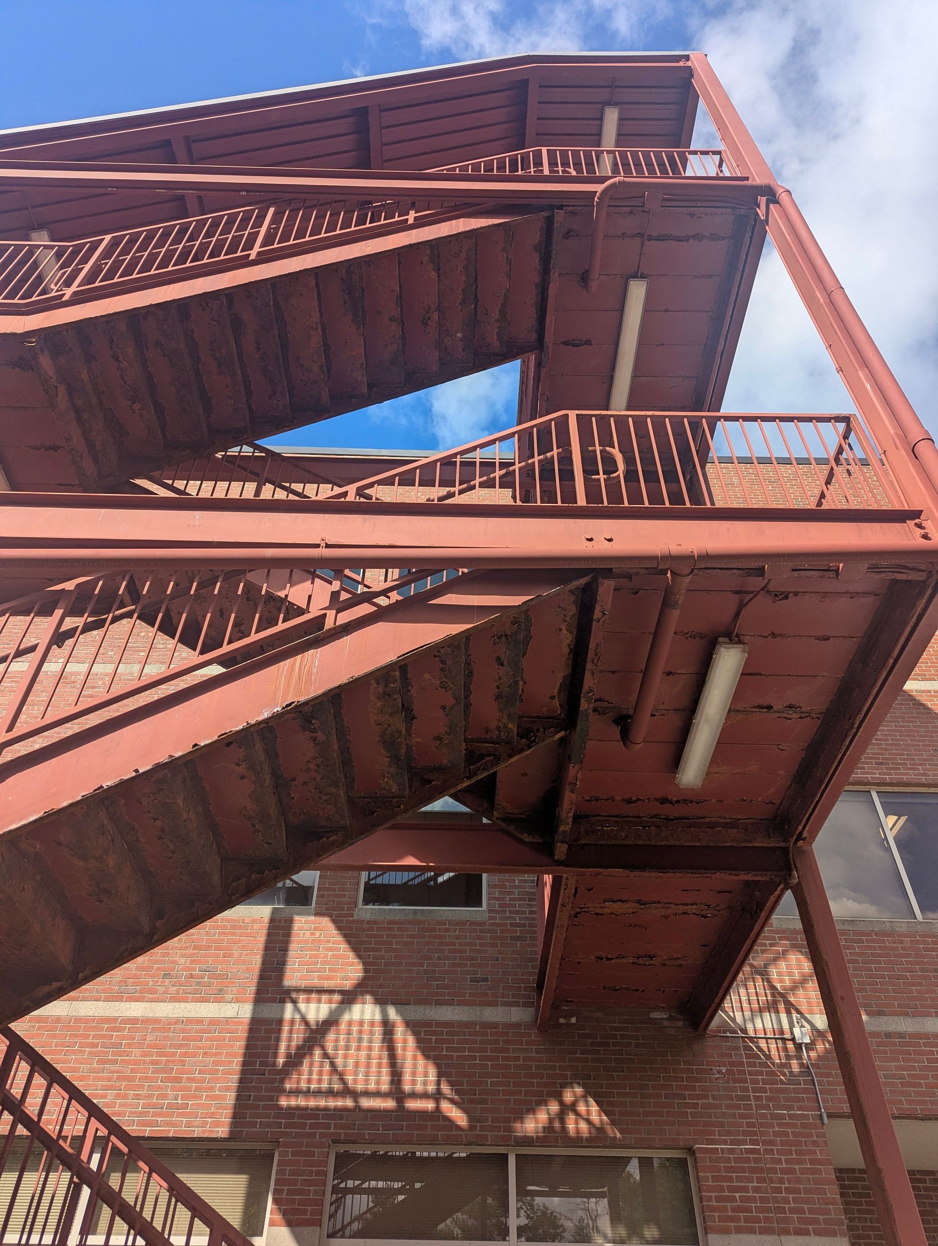 Red steel fire escape on a brick building, viewed from below against a blue sky.