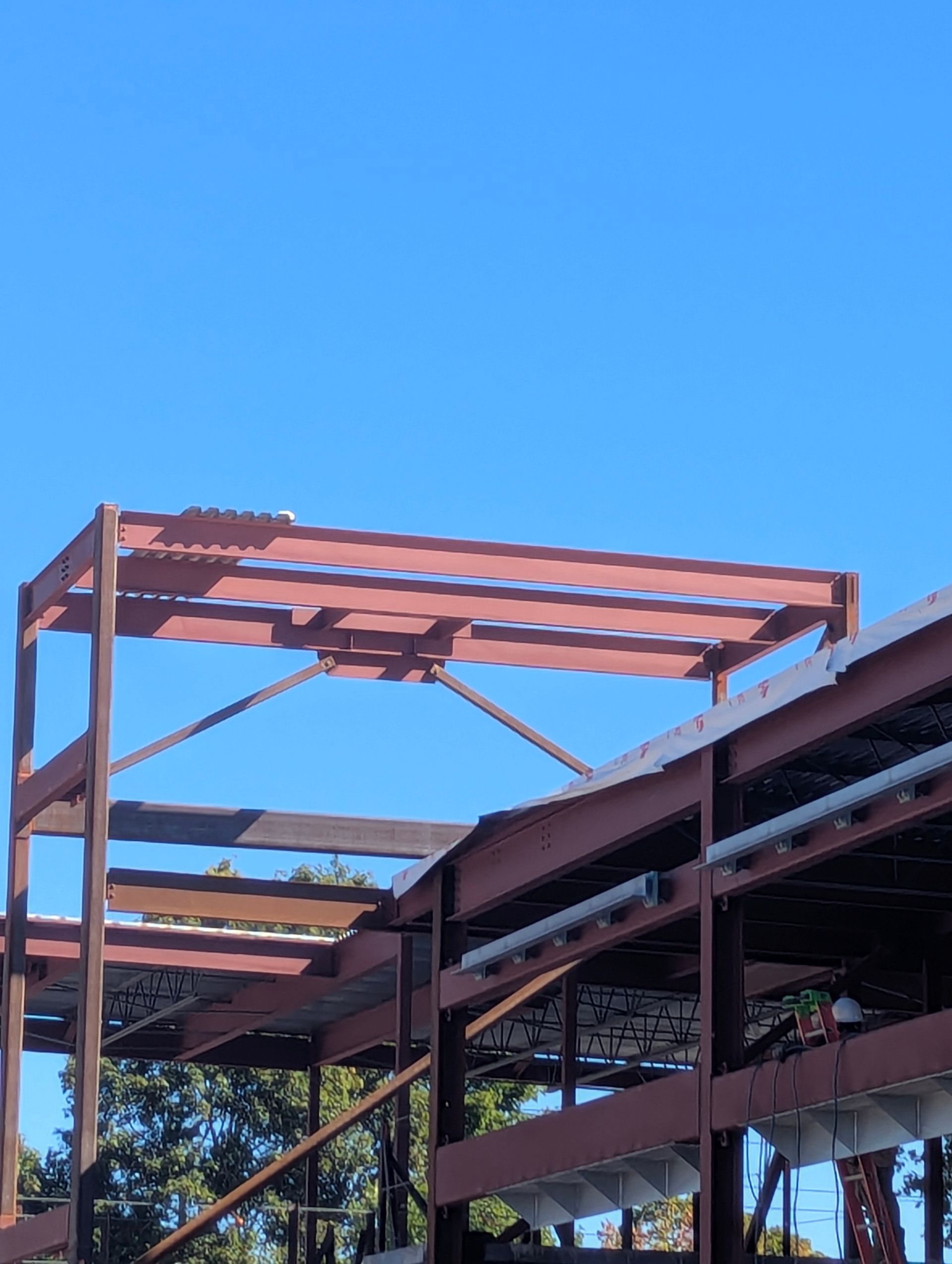 Partially built steel structure with red roof beams against a clear blue sky