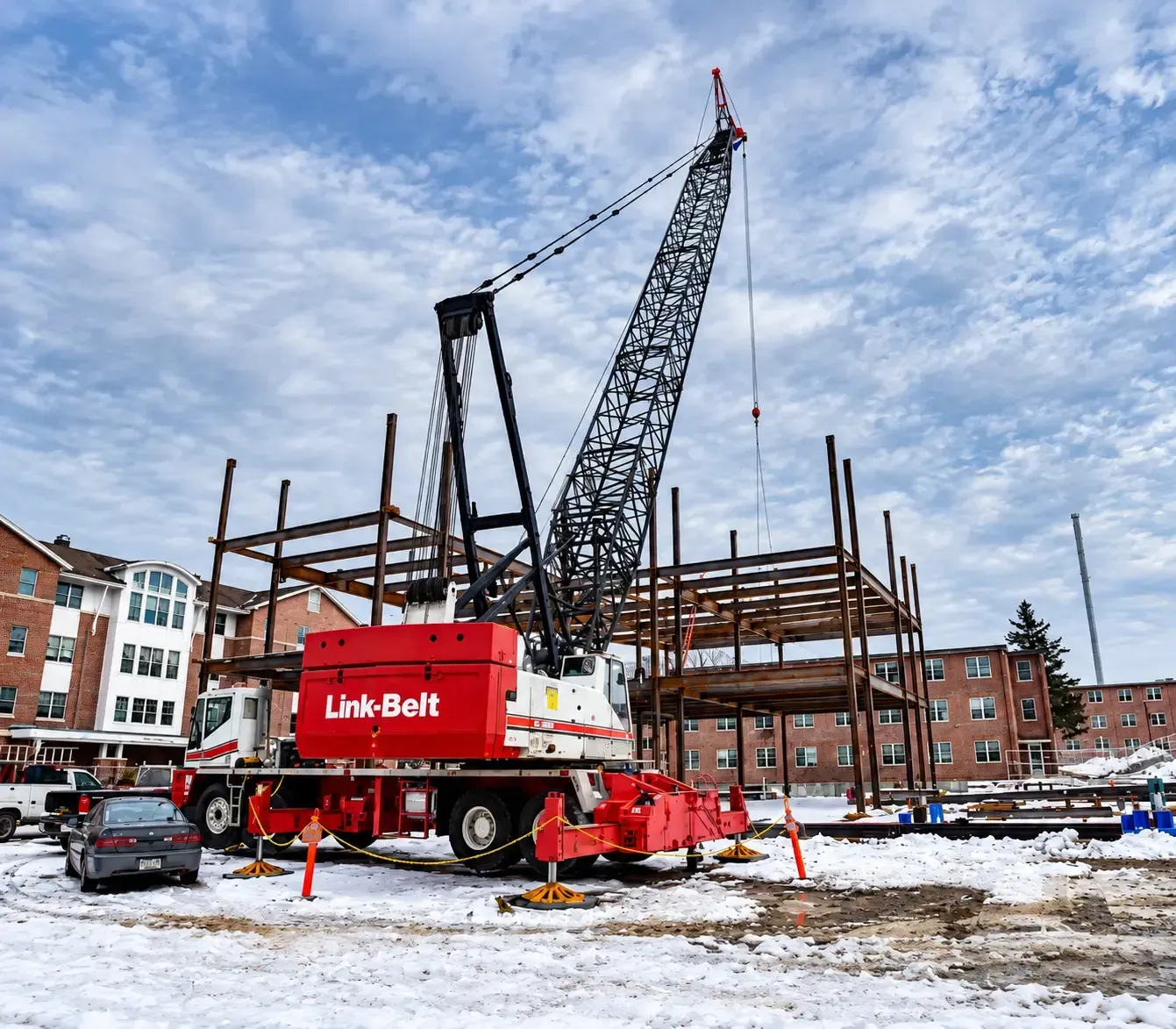 Red Liebherr crane at a snowy construction site beside a steel frame building under a cloudy sky