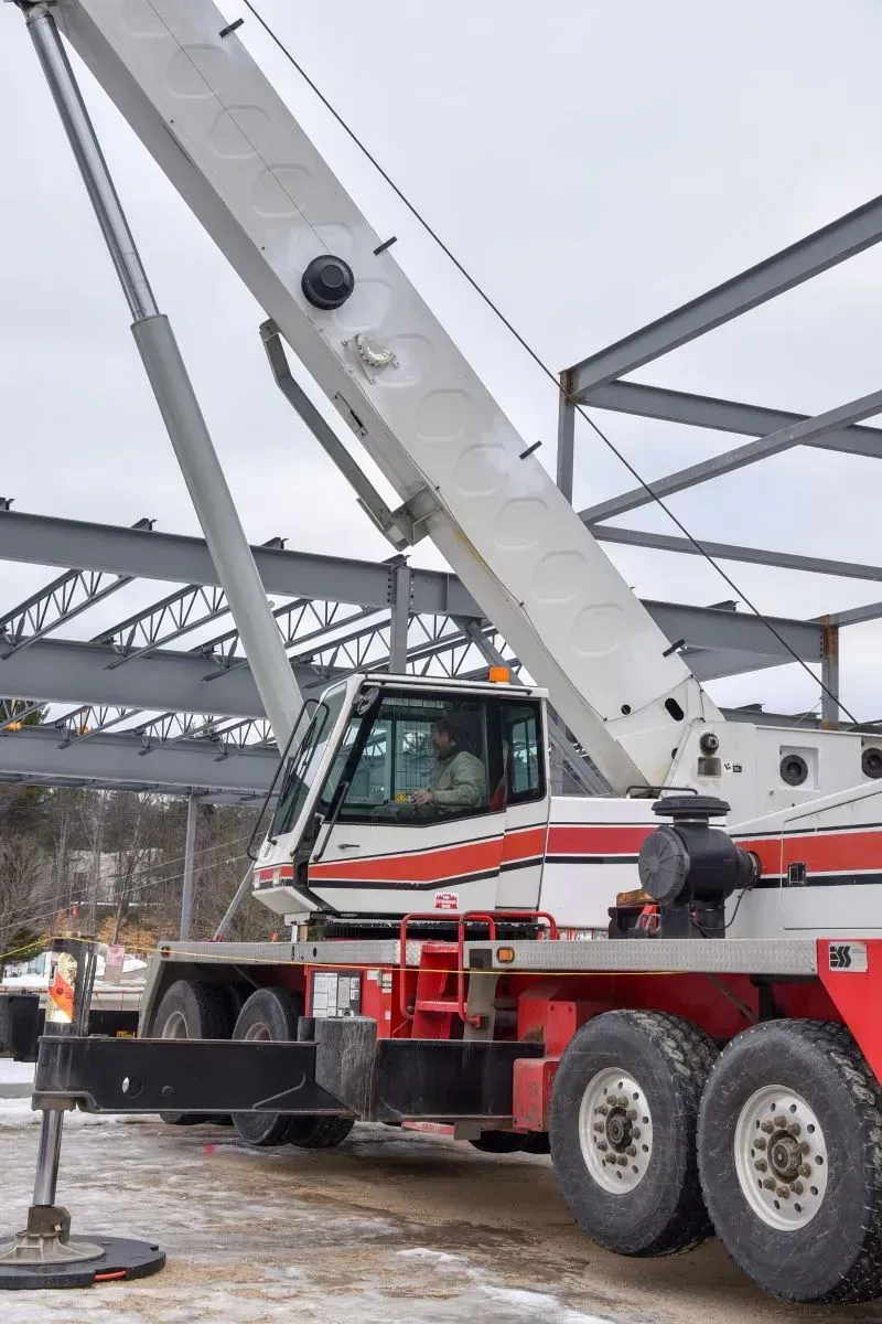 A red and white crane is parked in front of a building under construction.