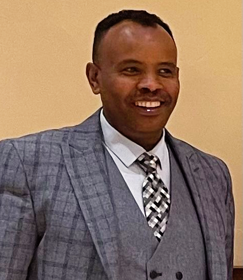 Man in gray suit smiles, facing right, against a neutral background.