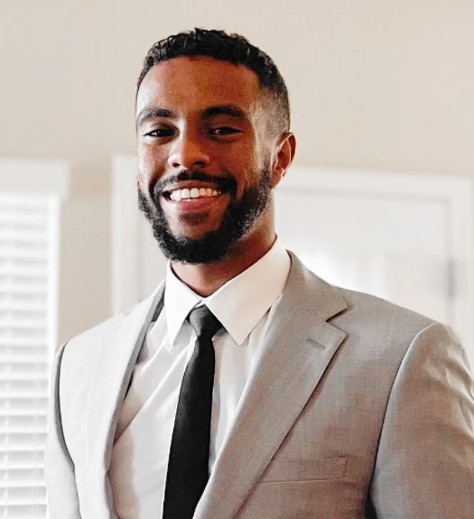 Man in light gray suit and black tie, smiling.