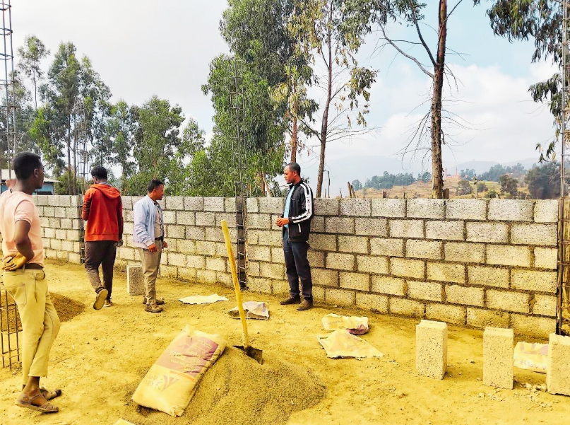 Men building a concrete block wall outdoors, with tools and materials nearby.