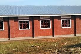 Red brick building with a blue metal roof and barred windows, set against a grassy area.