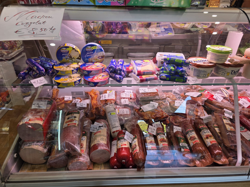 Vetrina piena di vari tipi di carne e formaggi confezionati in un mercato.