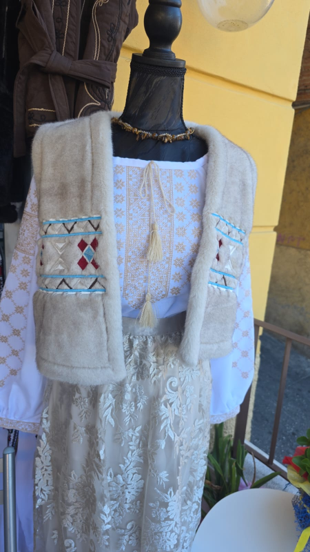 Manichino in abito tradizionale ucraino dai colori chiari: camicetta ricamata, gonna in pizzo e gilet di pelliccia.