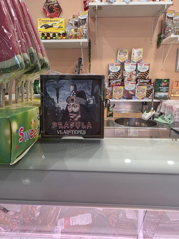 All'interno di un negozio, sul bancone è esposta un'immagine incorniciata di Vlad l'Impalatore, mentre sullo sfondo si vedono dolci e altri prodotti.