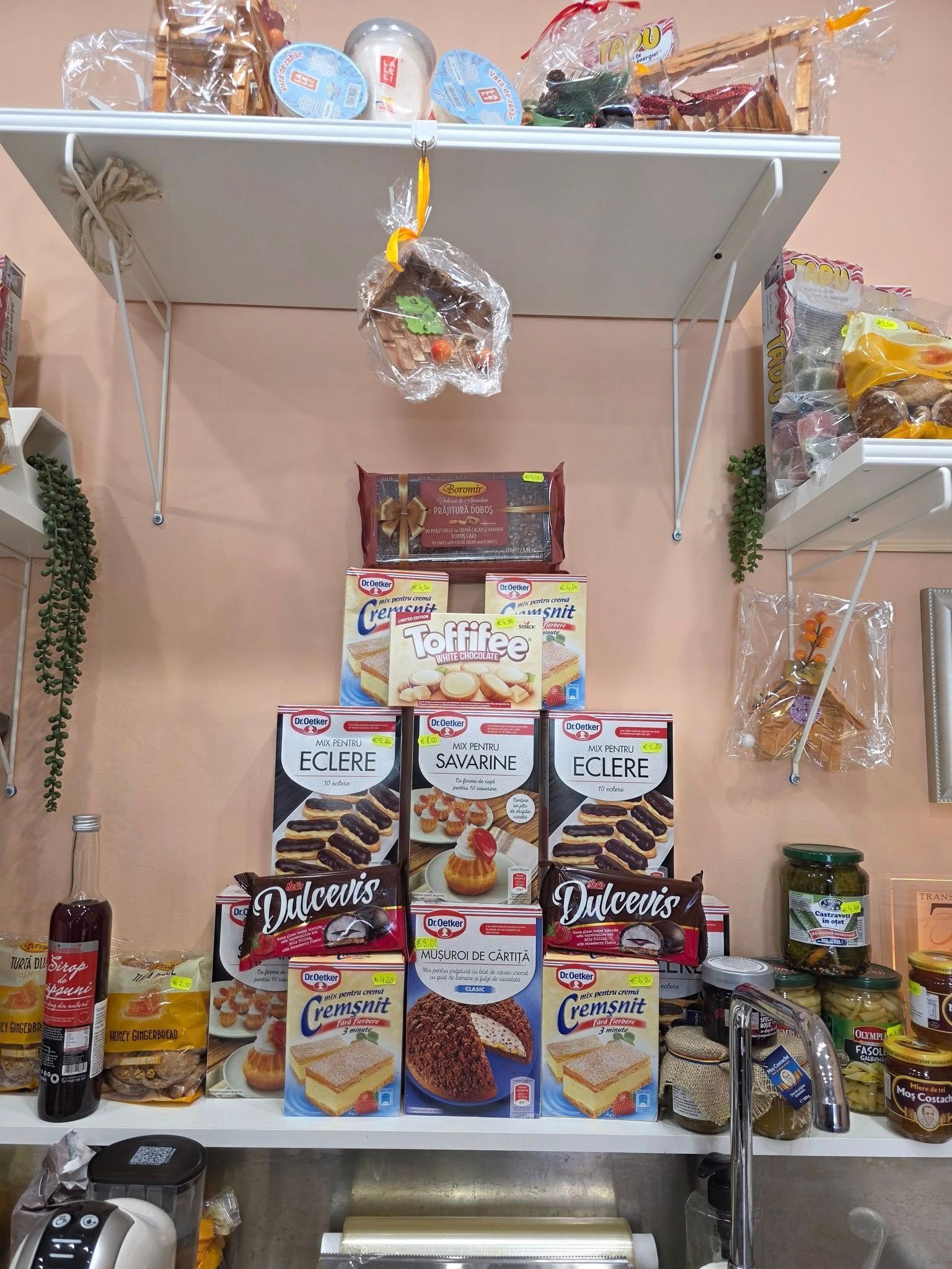 Esposizione sugli scaffali di vari prodotti alimentari confezionati: torte, biscotti e altri snack.