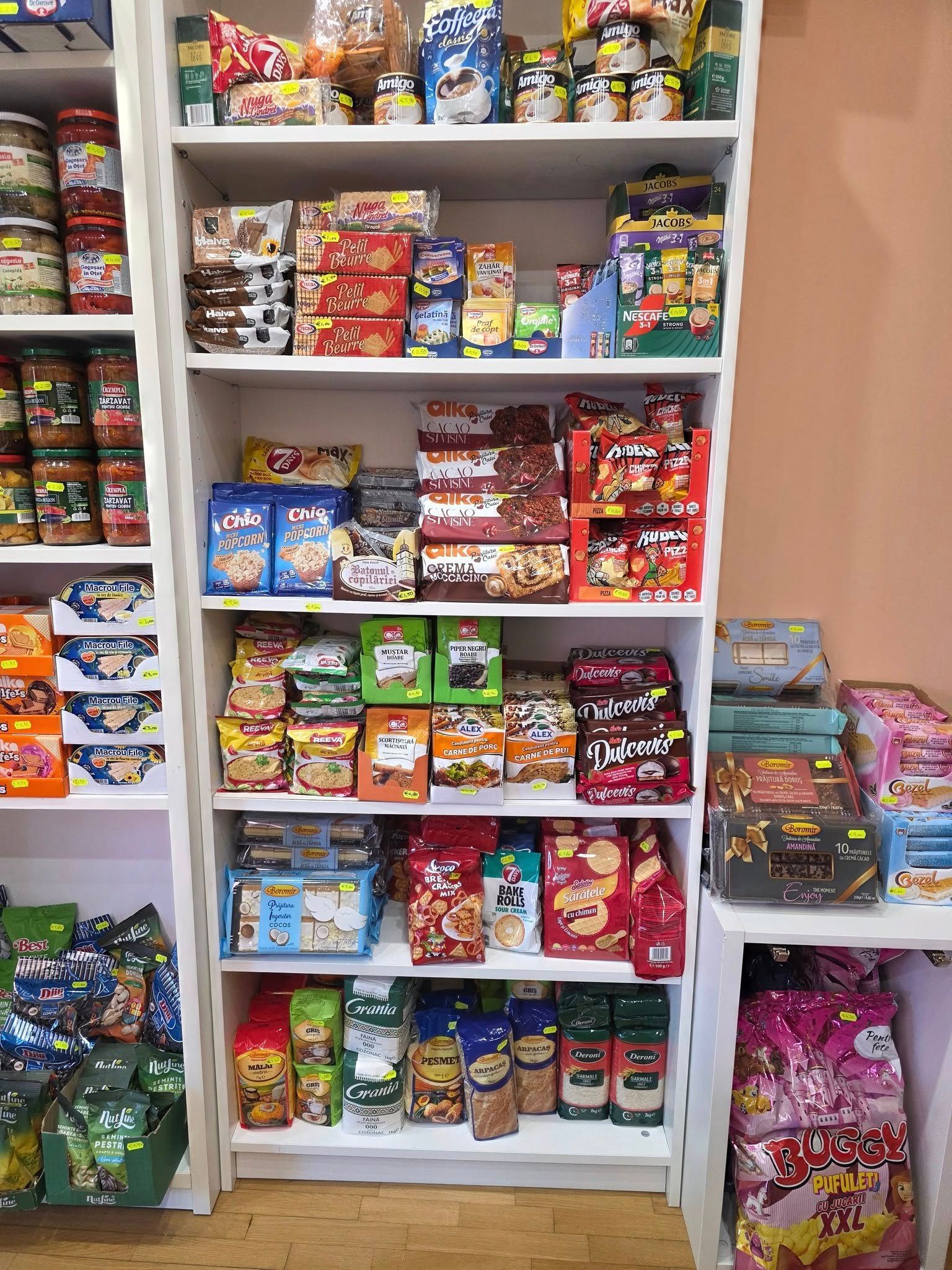 Scaffali pieni di vari snack confezionati, tra cui biscotti, cracker e caramelle, in un negozio.