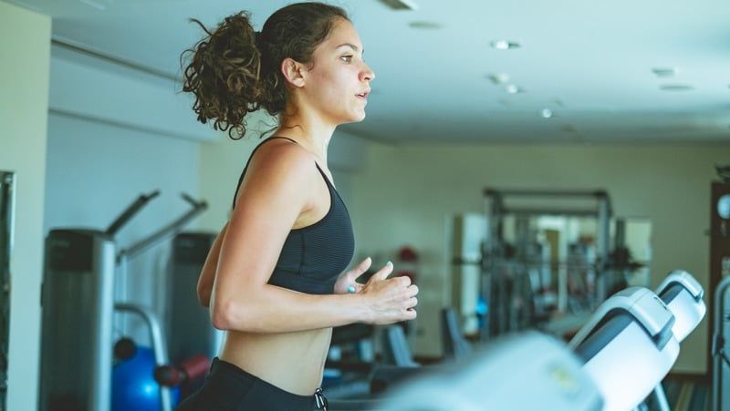 Woman with curly hair running on a treadmill in a gym.