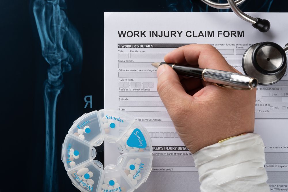 Hand Filling out A Work Injury Claim Form Beside an X Ray and Medicine — Rainbow Beach General Practice in Rainbow Beach, QLD