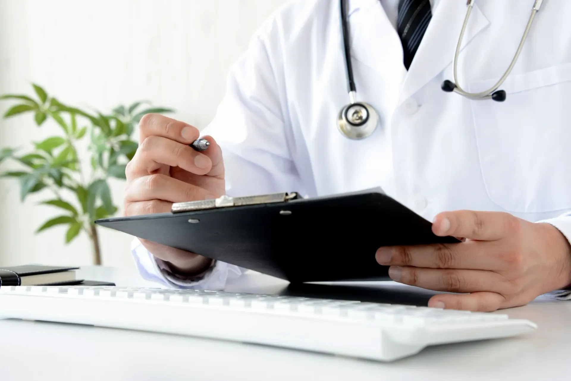 Doctor Holding a Clipboard at A Desk with A Keyboard and Plant — Rainbow Beach General Practice in Rainbow Beach, QLD