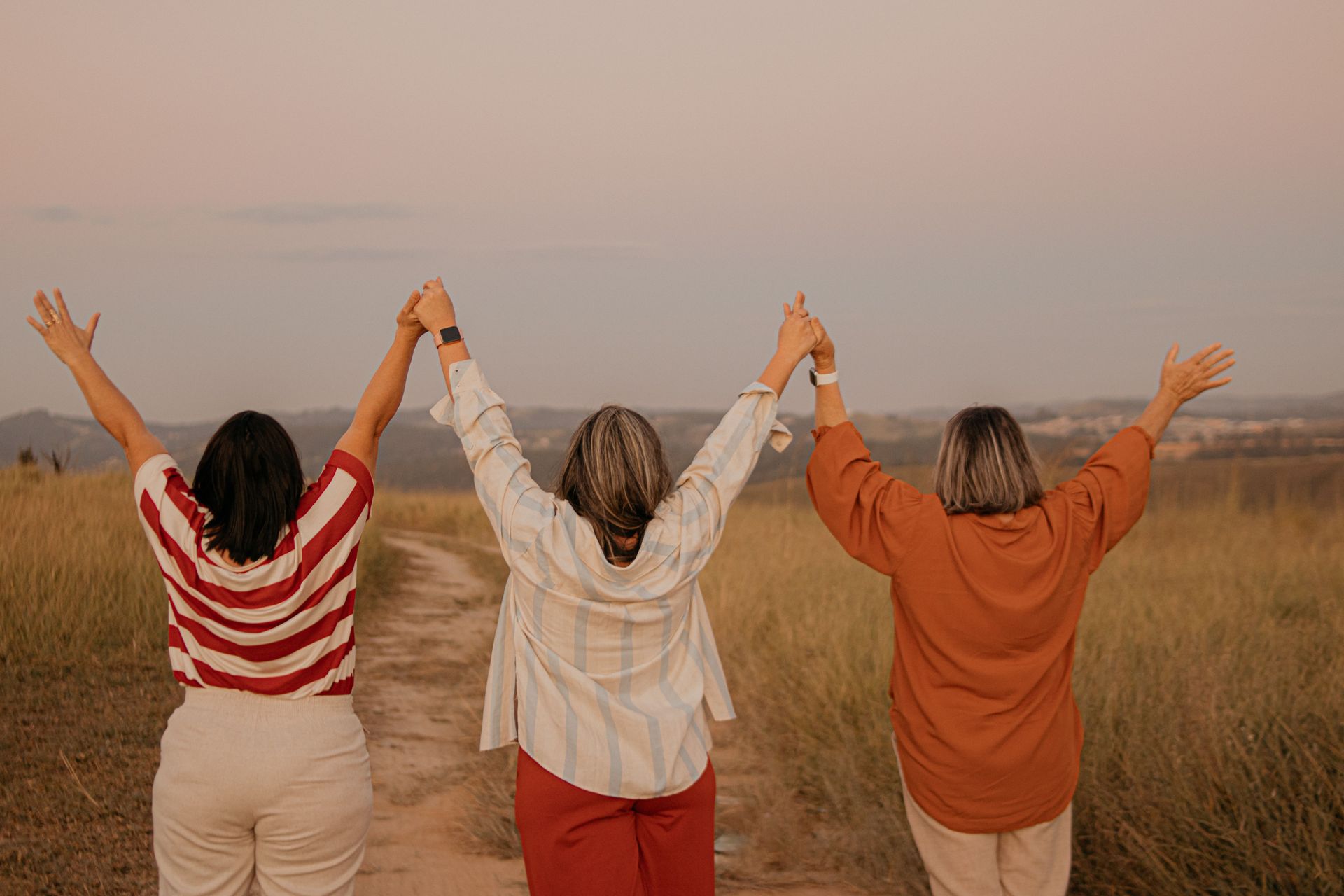 Three people with raised arms stand in a field at sunset. — Rainbow Beach General Practice in Rainbow Beach, QLD