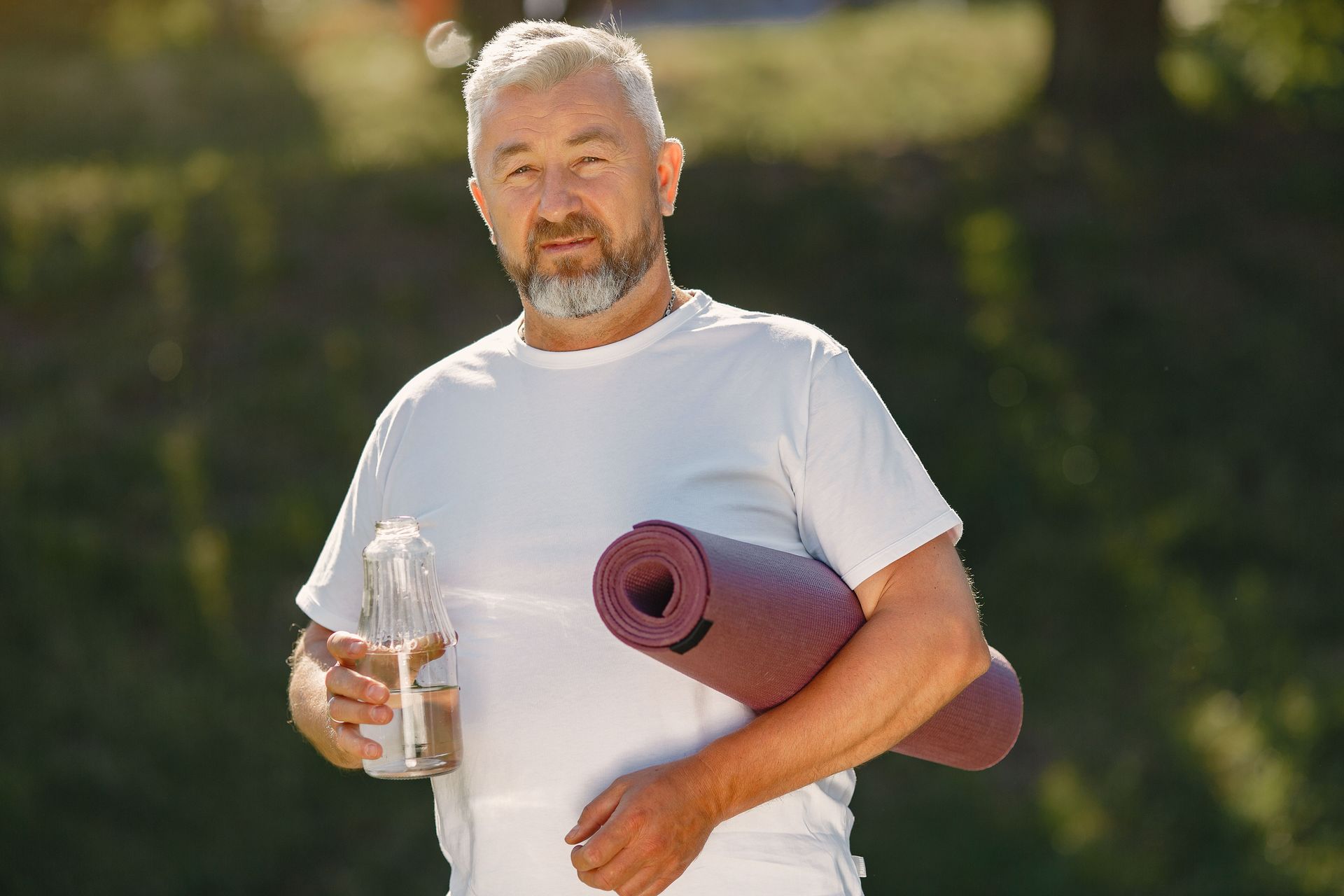 Man holding a water bottle and yoga mat outdoors in sunlight — Rainbow Beach General Practice in Rainbow Beach, QLD