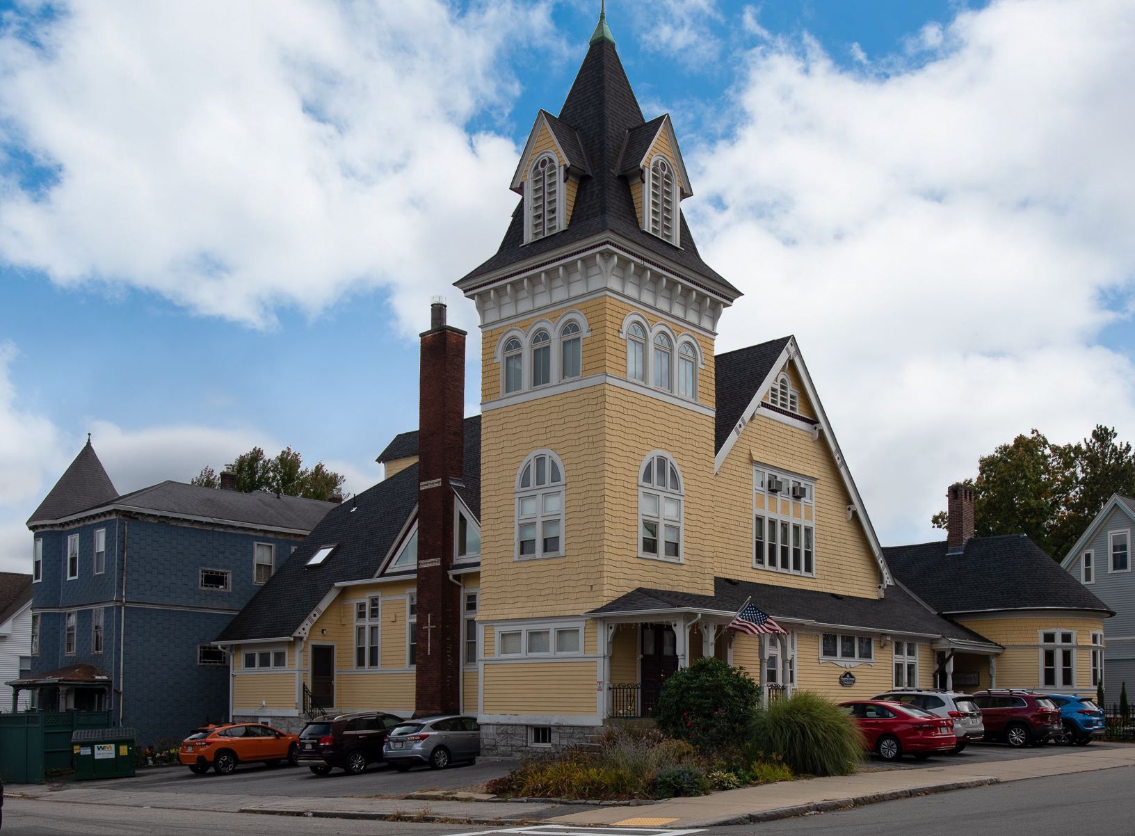 A large yellow building with a tower and cars parked in front of it