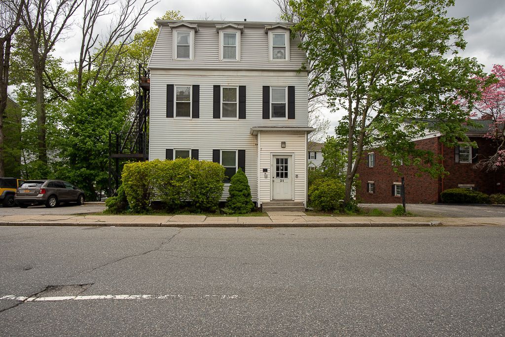 A white house with black shutters sits on the corner of a street