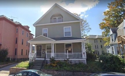 A large house with a porch and a car parked in front of it.