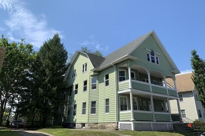 A large green house with a porch is surrounded by trees.