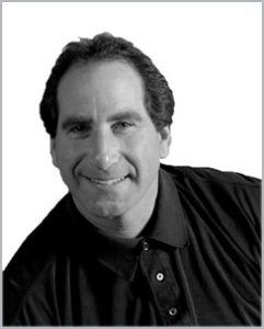 Black-and-white portrait of a smiling man in a dark shirt against a plain background