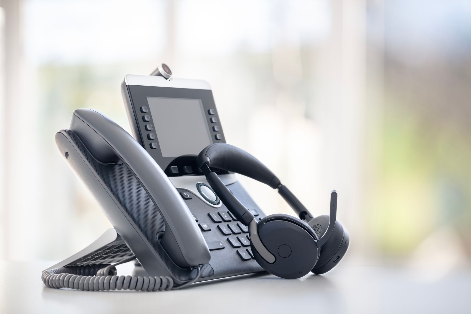 Close-up of a gray office desk phone with keypad and coiled cord