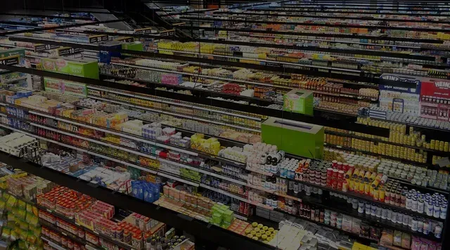 Corredor de supermercado com longas prateleiras de produtos alimentícios embalados e itens coloridos dispostos lado a lado.