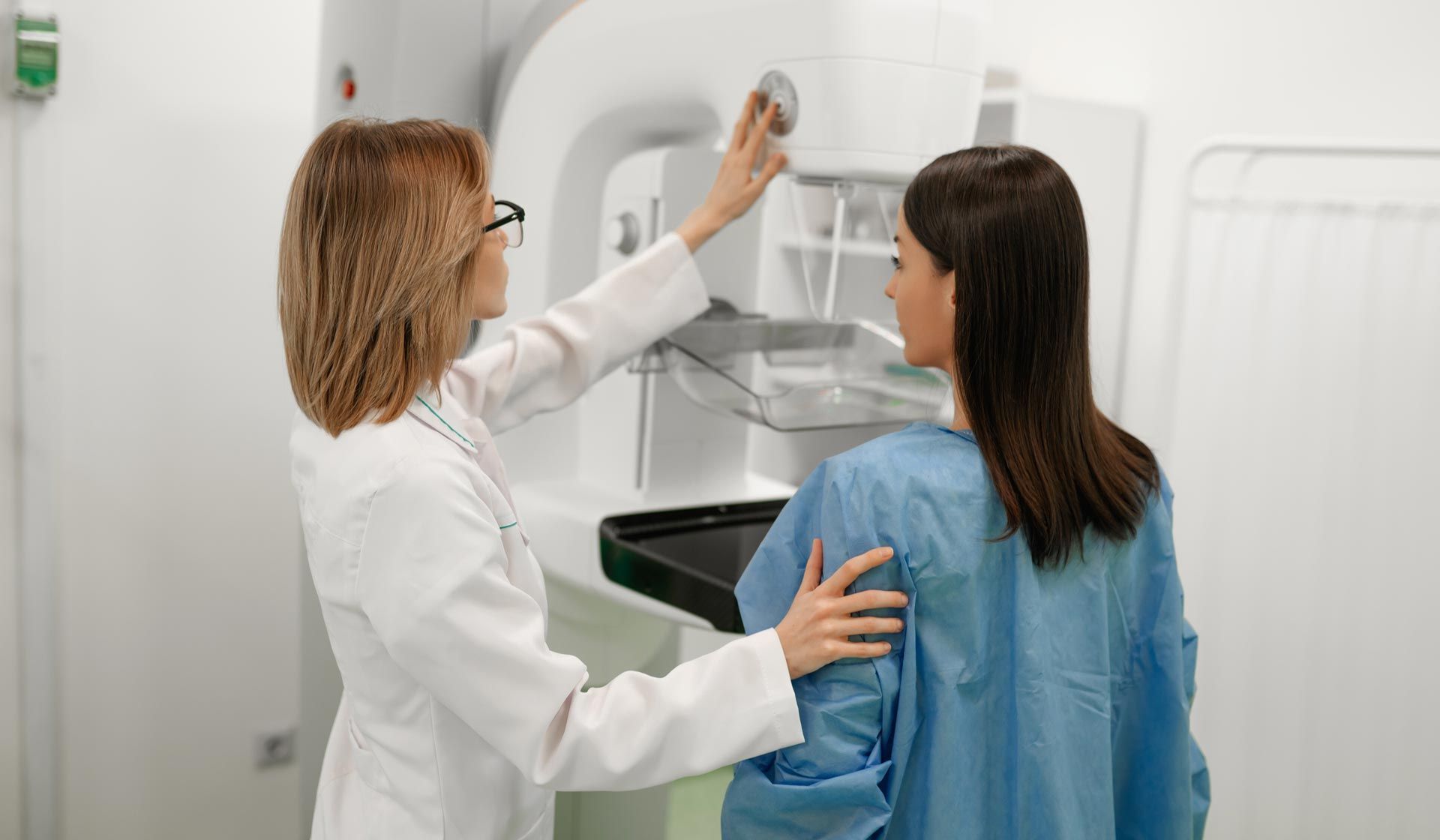 A female doctor assists a patient in a blue gown during a mammogram screening