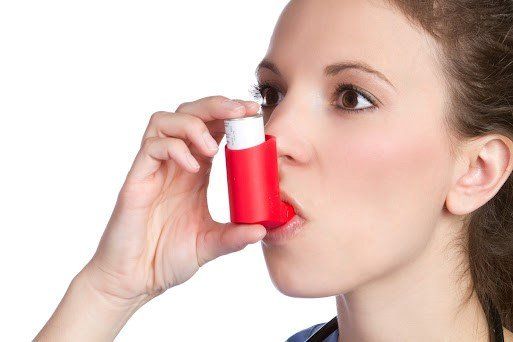 Woman using a red asthma inhaler to inhale medication, white background.