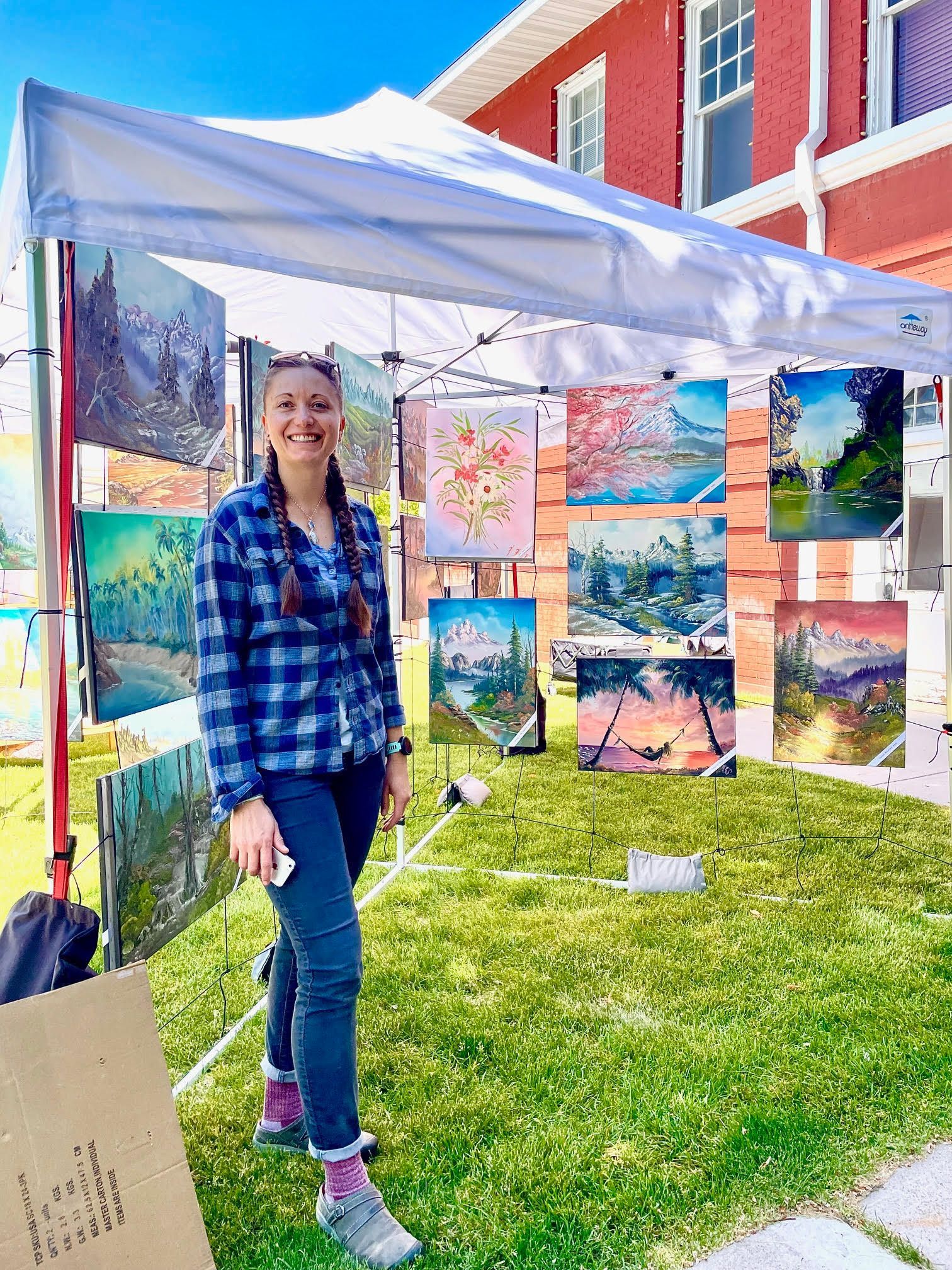 A woman is standing in front of a tent with paintings on it.