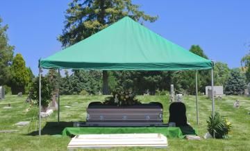 Green canopy tent over benches in a sunny park with trees and gravestones in the background