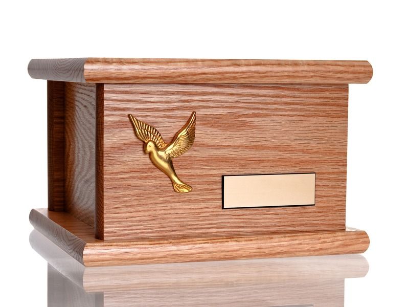 Wooden urn with a gold bird emblem and a blank nameplate on a reflective surface