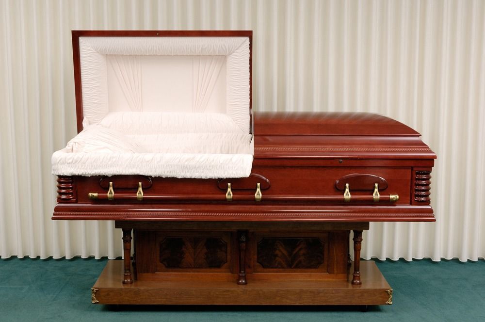Wooden casket with open white-lined lid on a stand, set against a striped wall.