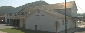 White building with a sign near a hillside road under a bright sky