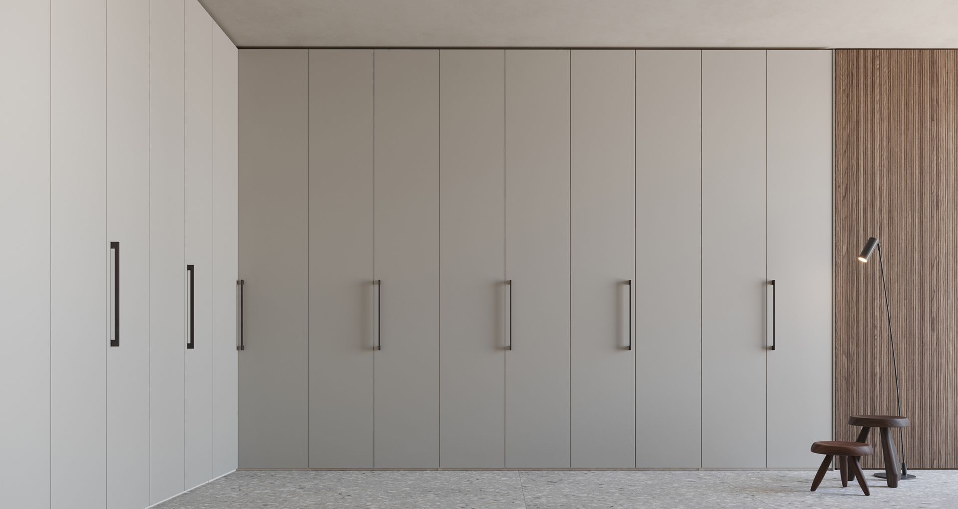 Ampio armadio grigio moderno con maniglie verticali, accanto a pannelli in legno, uno sgabello e una lampada.