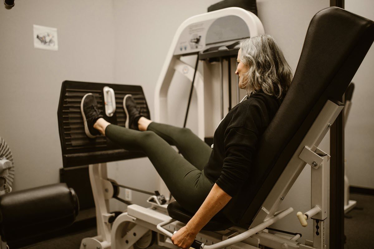 A person in a black shirt and green leggings performs a leg press exercise on a machine at a gym.