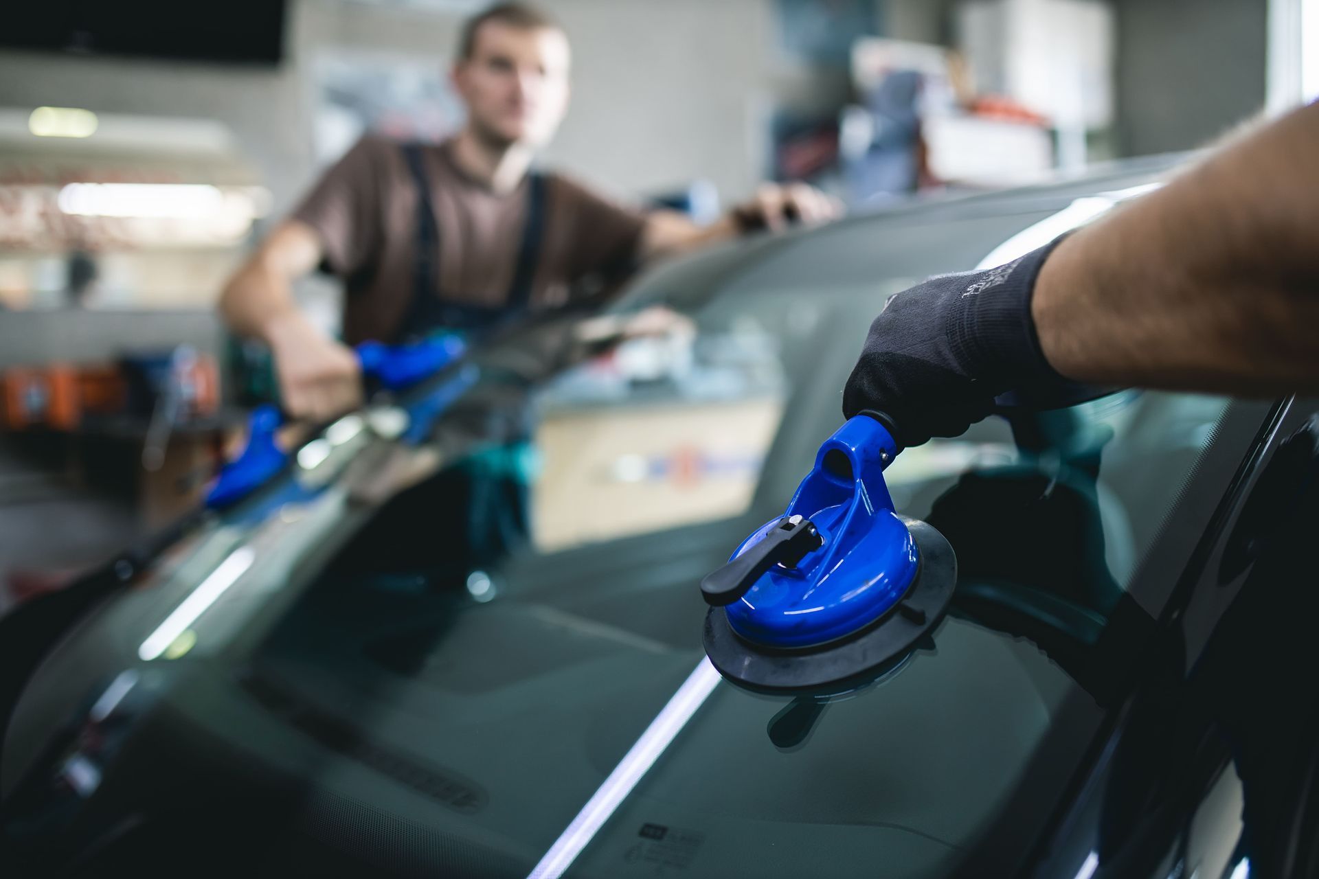 Two auto technicians installing a windshield using suction cups in a garage.