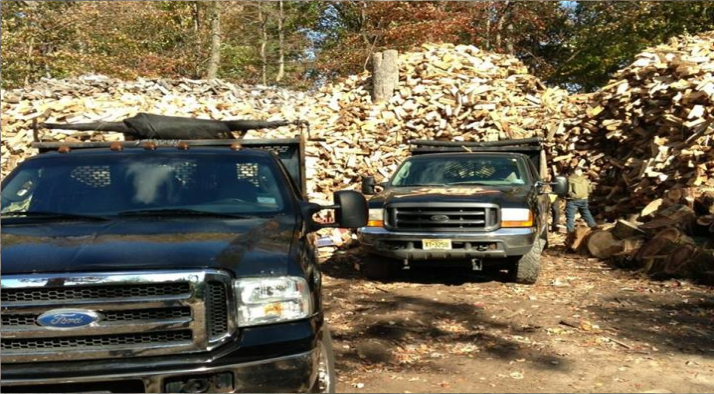 Two pickup trucks on a dirt road in front of large piles of wood debris